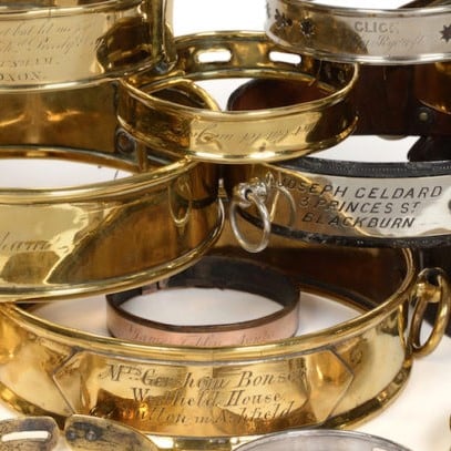 Close-up of vintage brass and metal dog collars with engraved names and address details