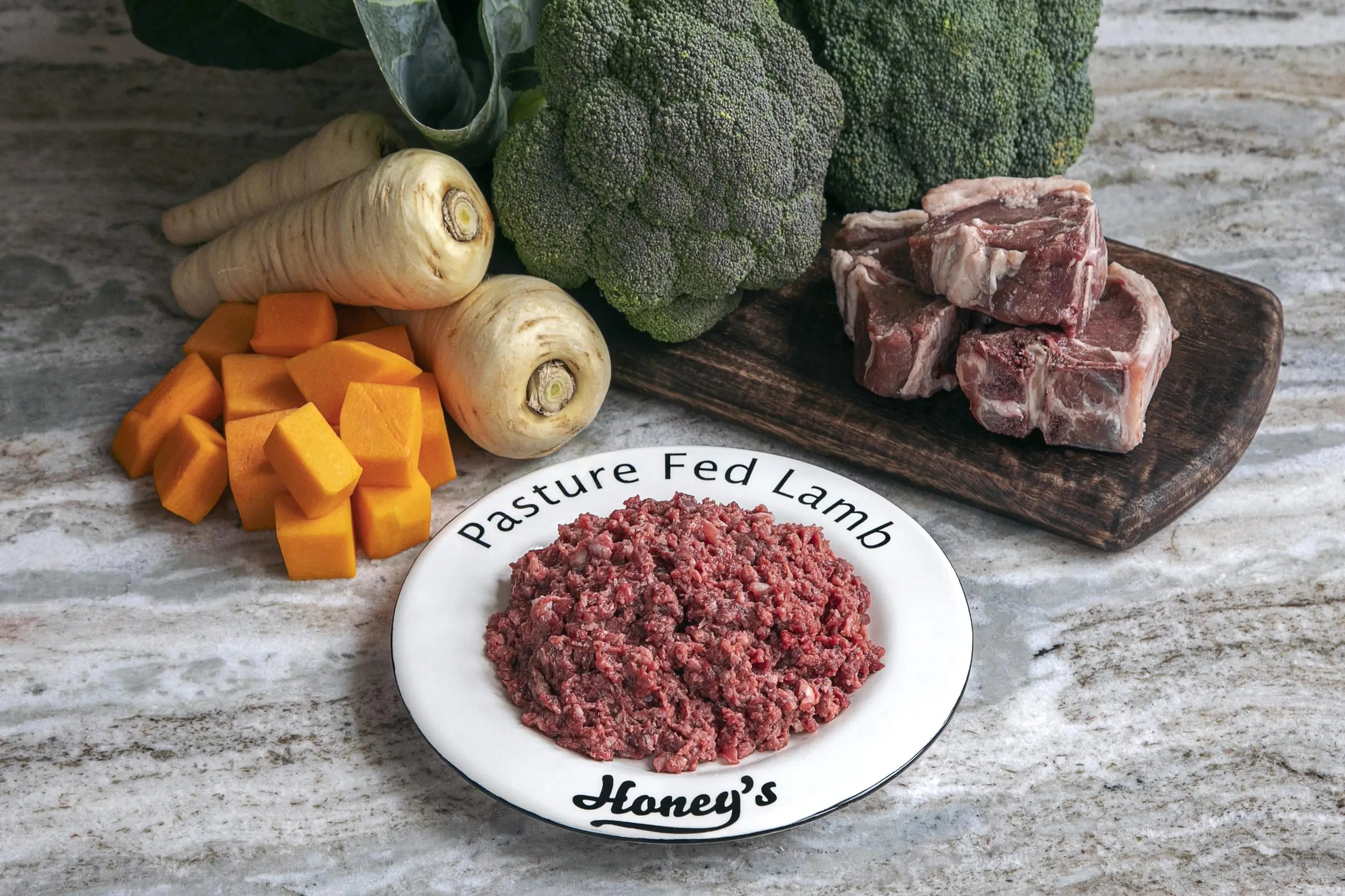 Plate of pasture fed lamb mince surrounded by broccoli, parsnips, butternut squash, and lamb chops on a marble surface