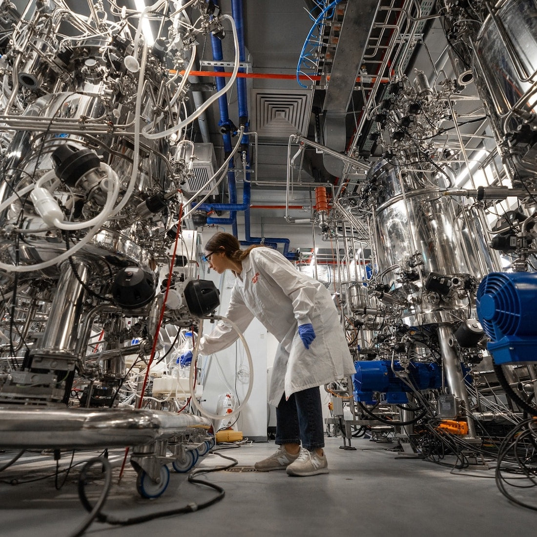 Scientist in white lab coat working with stainless steel bioreactors in synthetic meat laboratory