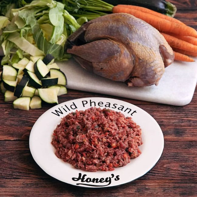 Raw whole wild pheasant with fresh carrots, zucchini, and chopped greens on cutting board, ground pheasant in bowl