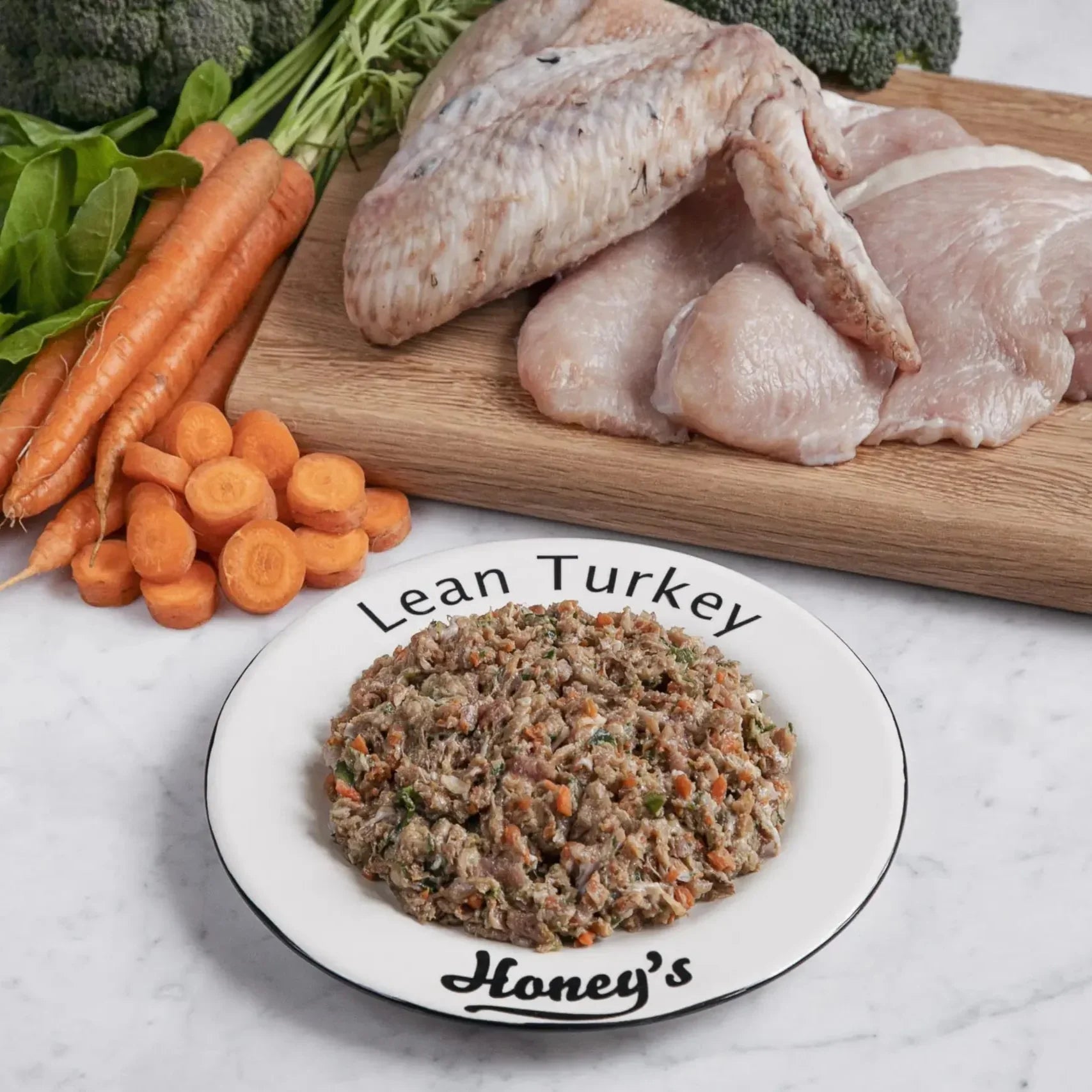 Fresh lean turkey meat and wing on cutting board with carrots and broccoli next to a plate of lean turkey mixture