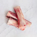 Three raw beef short ribs stacked on a white marble surface, showing marbled red and white meat