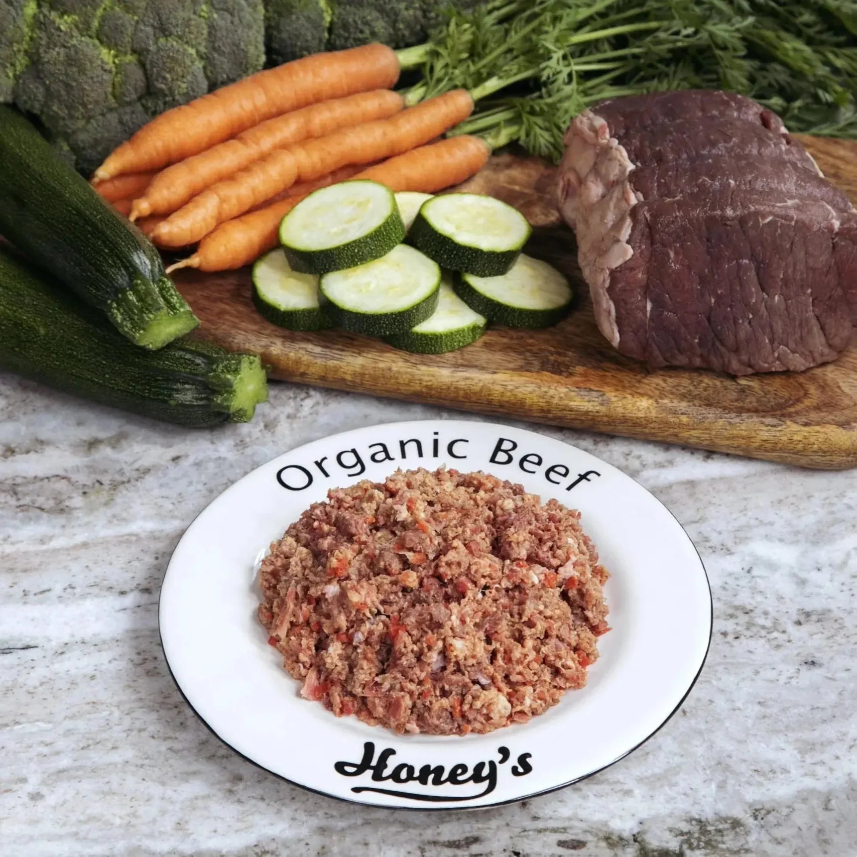 Plate of organic ground beef with fresh carrots, zucchini, and raw beef on wooden cutting board